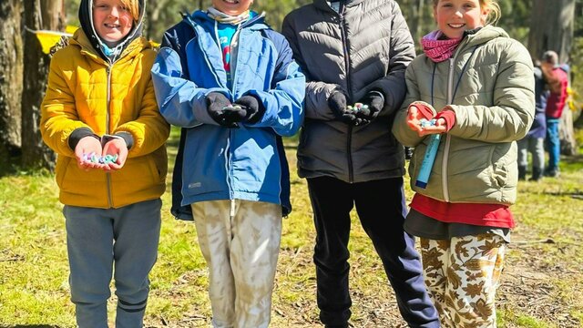 Easter Egg Hunt Four kids smiling at the camera as they show off the Easter eggs they found