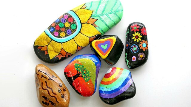 River rocks decorated in brightly coloured hand drawn images of flowers, trees, rainbows and pattern