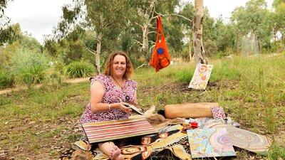 A woman with art supplies sitting on a green hill.