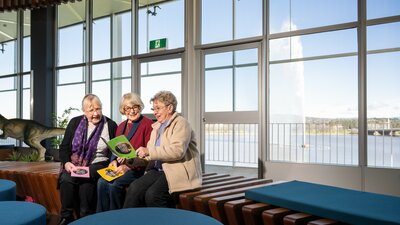 Three ladies reading from traveller brochures at a visitor centre.