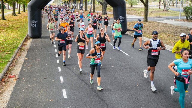 Canberra Marathon Running Runners taking part in the Canberra Marathon, running on a road under an inflatable archway with trees on both sides of the road.
