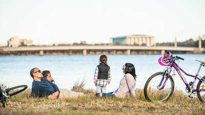 A couple with two young kids relaxing next to their bikes near the lake.
