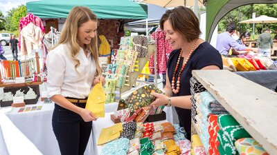 Woman buying a necklace from a market stall outside.