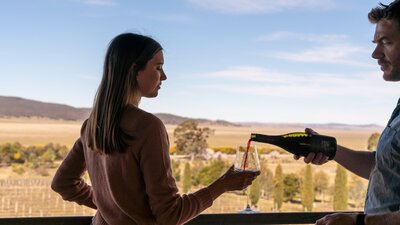 A man pouring red wine into a woman's glass as they look out over Lerida Estate Winery.