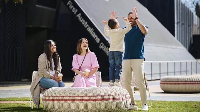 Family fun at the National Museum Canbera Two women sit outside and a man stands and high fives a young boy at the National Museum of Australia.