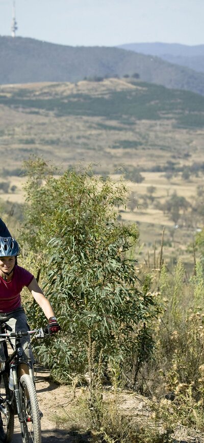 A few friends mountain biking with a view of Canberra and Telstra Tower in the background.