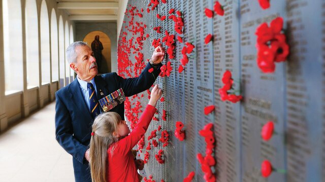 A young child and an older man placing a poppy into the wall of names of fallen soldiers.