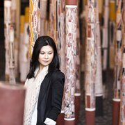 A woman in a black blazer walking between indigenous memorial poles.