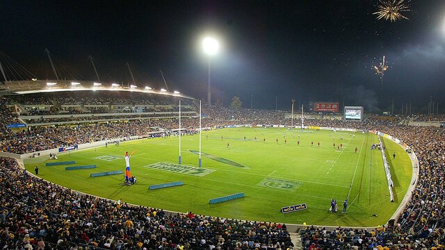 A large crowded stadium at night with a rugby game.