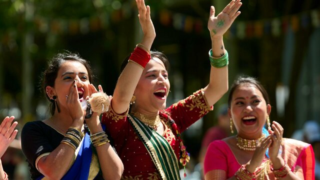 Celebrate with us at the 2024 National Multicultural Festival! Three women in cultural dress clap for the festival parade performers