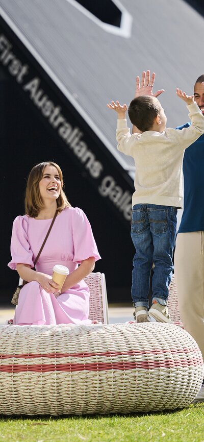 Family fun at the National Museum Canbera Two women sit outside and a man stands and high fives a young boy at the National Museum of Australia.